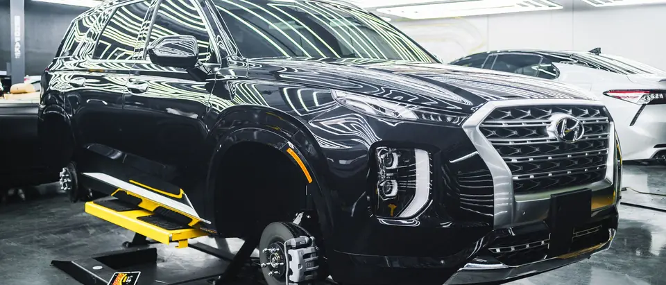 Dark SUV on a wheel alignment rig in a bright shop