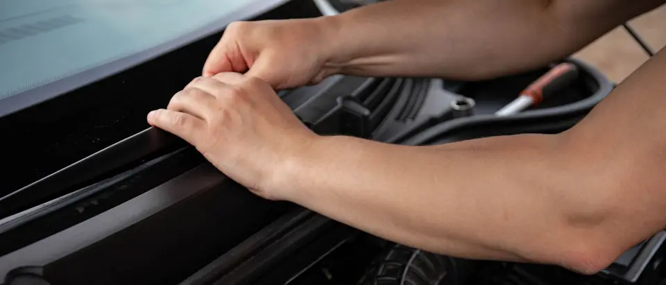 Hands pressing the cowl trim into place at the foot of a windshield